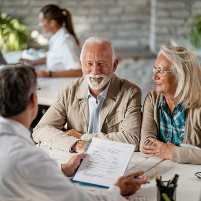 Happy senior couple communicating with a doctor about their health insurance while going through paperwork.